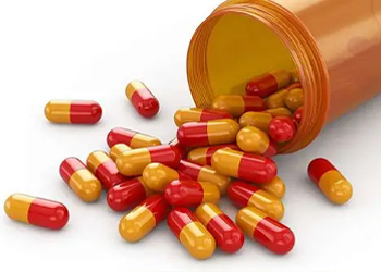 Red-orange hard capsules pouring out from medicine bottle