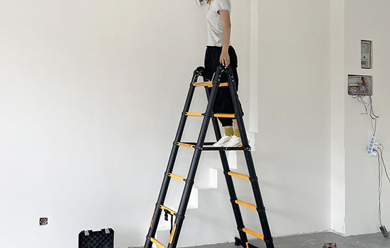 woman standing on a telescopic a frame ladder is painting the wall