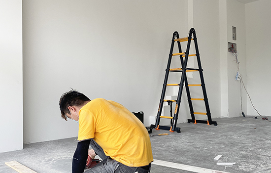 The renovation worker is installing the floor and there is a telescopic ladder next to him