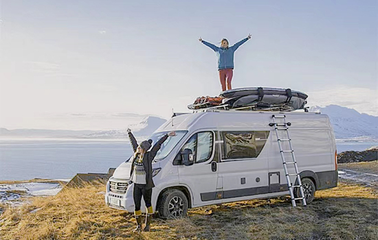 une fille se tient sur le dessus du camping-car et agite les mains après avoir grimpé avec une echelle telescopique tente de toit