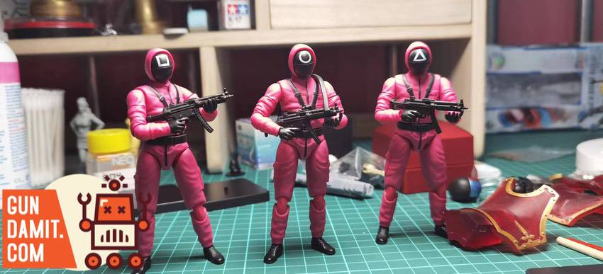 Red Suit 1/18 Squid Game three pink soldiers holding guns on workbench Red Suit 1/18 Squid Game three pink soldiers holding guns on workbench