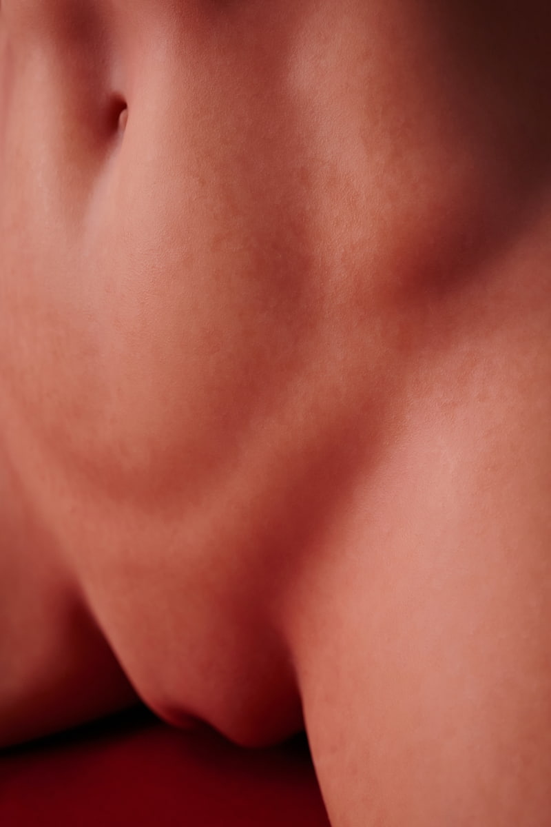 ULW 663# Emma: This extreme close-up view focuses on the doll's abdominal section, detailedly showcasing her neat navel and smooth, realistic skin texture with lifelike fine pores and subtle skin grain against a red backdrop.