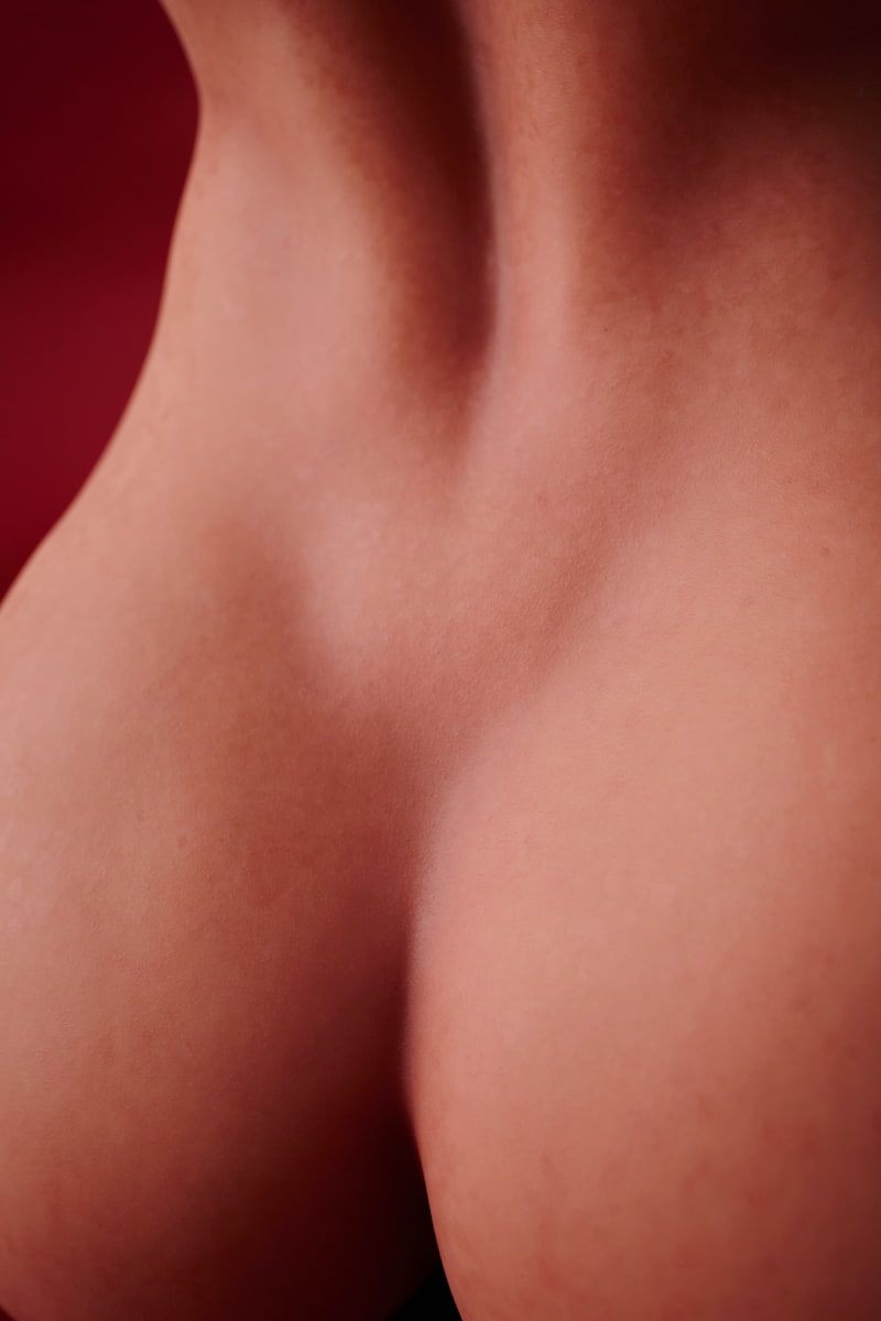 ULW 663# Emma: This close-up view focuses on the lower back and upper cleft of the doll's naked torso, beautifully detailing the subtle indentation of her spine and smooth, realistic skin texture with natural fine grain against a red backdrop.