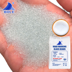Hand holding AASHTO M247 I Reflective Glass Beads, demonstrating their smooth, spherical texture and readiness for use in thermoplastic road marking paint.