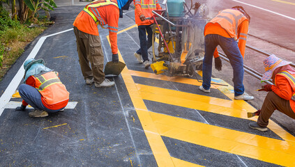 Worker applying thermoplastic road marking paint on asphalt surface during daytime construction