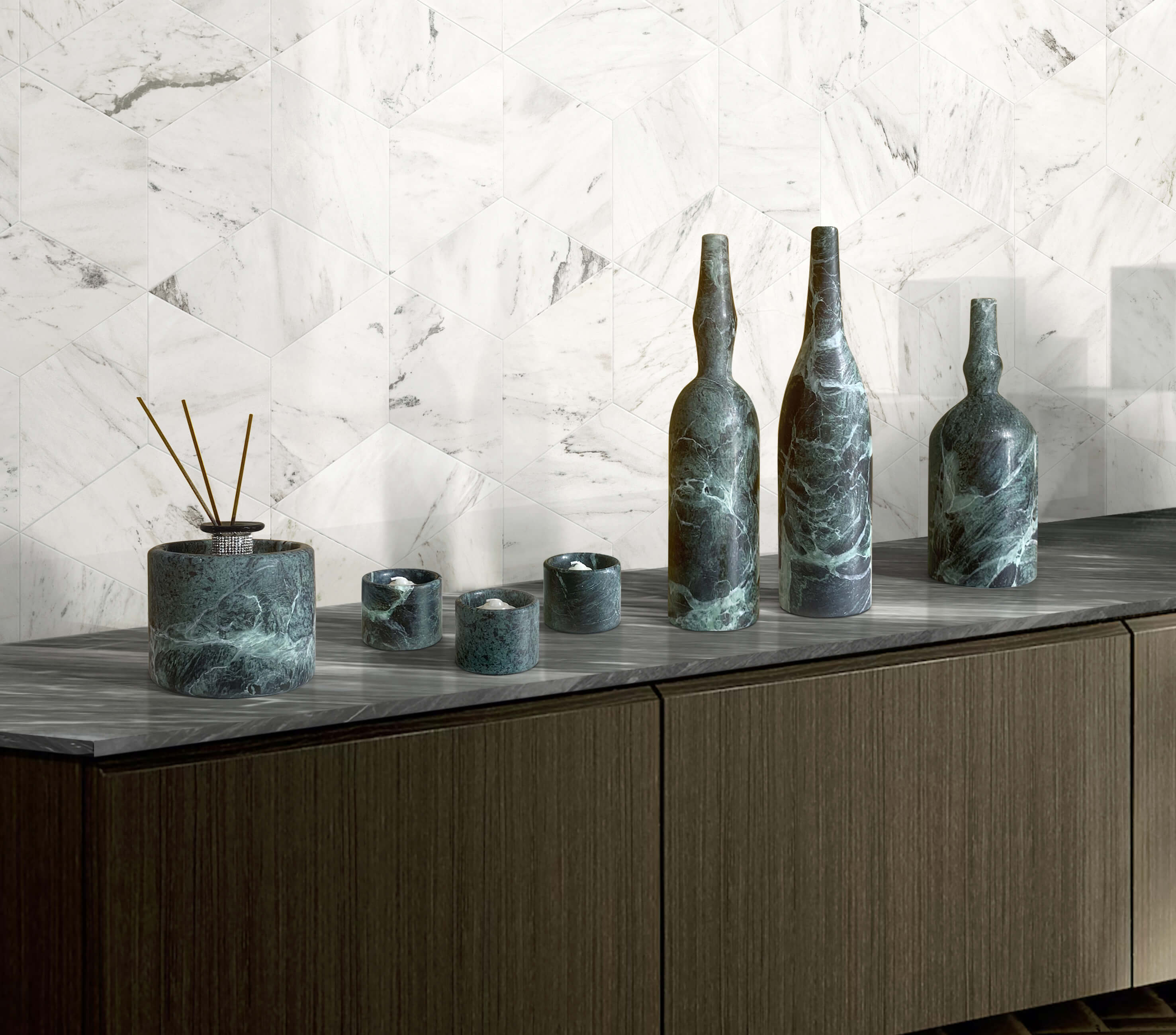 Close-up interior design detail of the luxury dark green marble sculptural vases and holders, highlighting the striking contrast with a bright white geometric tile background.