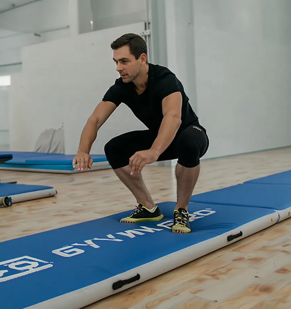 Parkour athlete landing on a thick, durable tumble track mat for safe, high-impact jump training in a martial arts studio.