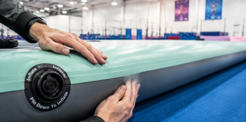 Close-up of a business buyer inspecting the premium PVC material, airtight seams, and valve quality of an imported gymnastics air track sample