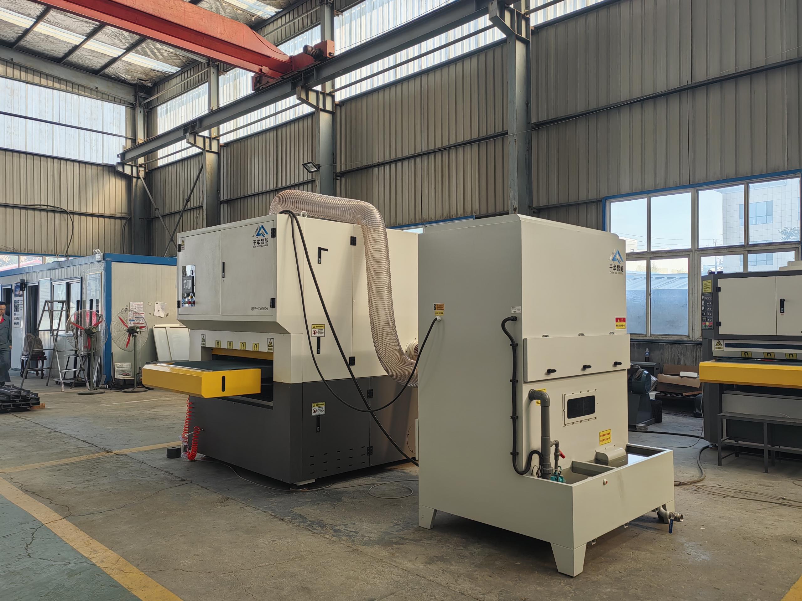Metal finishing machine with a connected extraction hose and adjacent collection unit in the workshop.