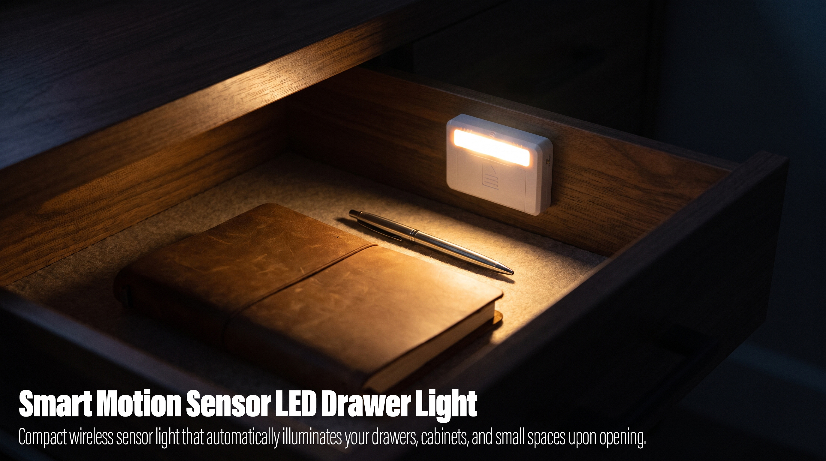 A small rectangular white wireless motion sensor LED light mounted inside an open wooden desk drawer, casting a warm glow onto a leather notebook and a silver pen.