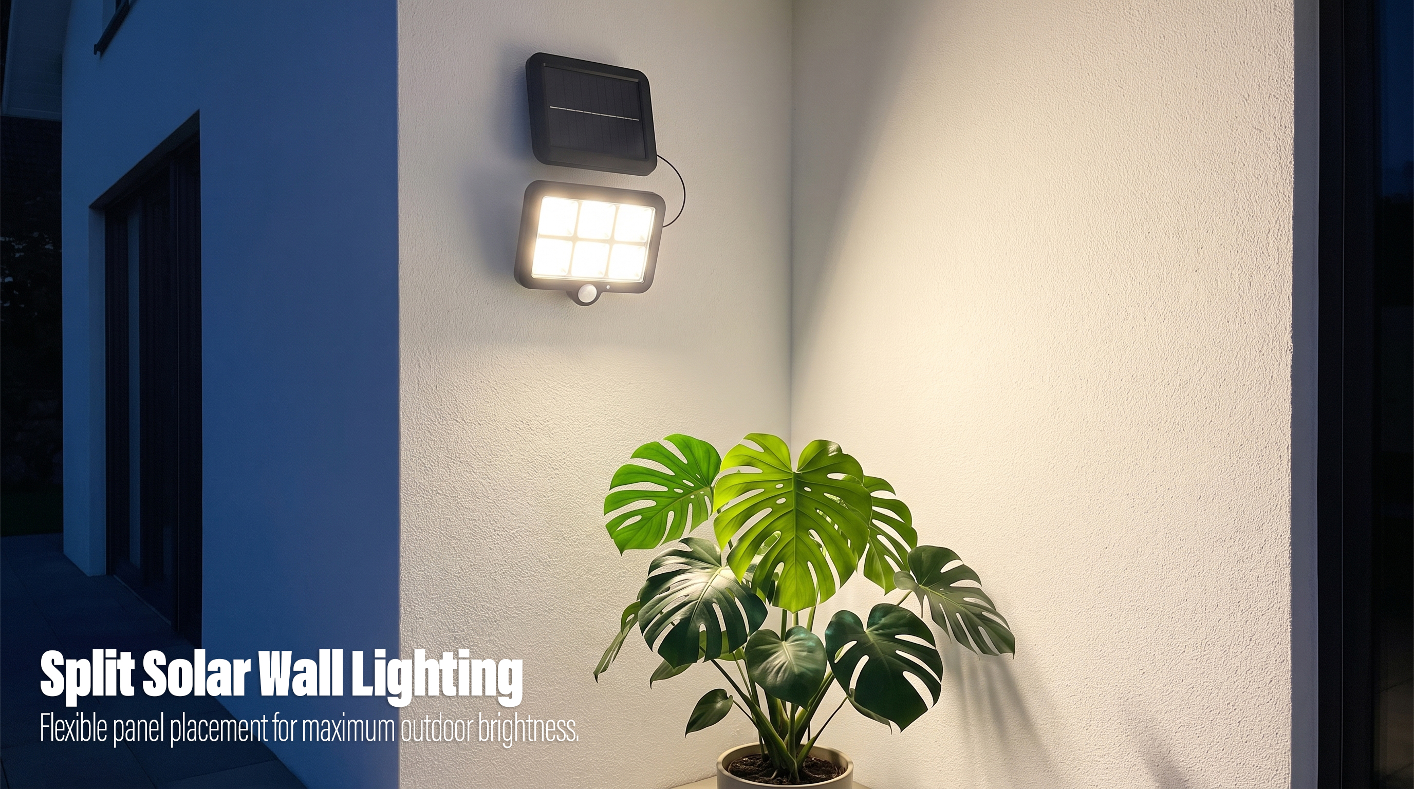 A split solar motion sensor flood light mounted on a white exterior wall glowing warmly over a potted plant at night.