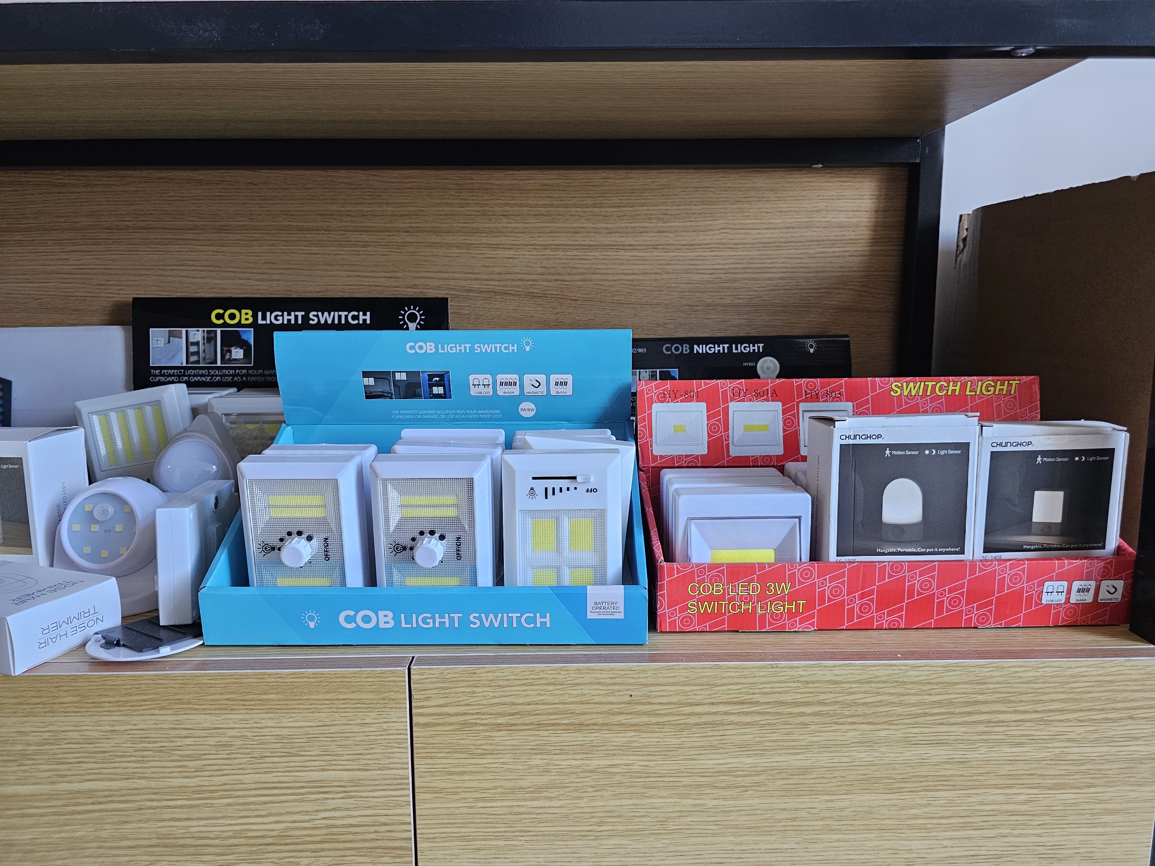 COB LED light switches and wall night lights packaged in colorful counter display boxes on a wooden shelf.
