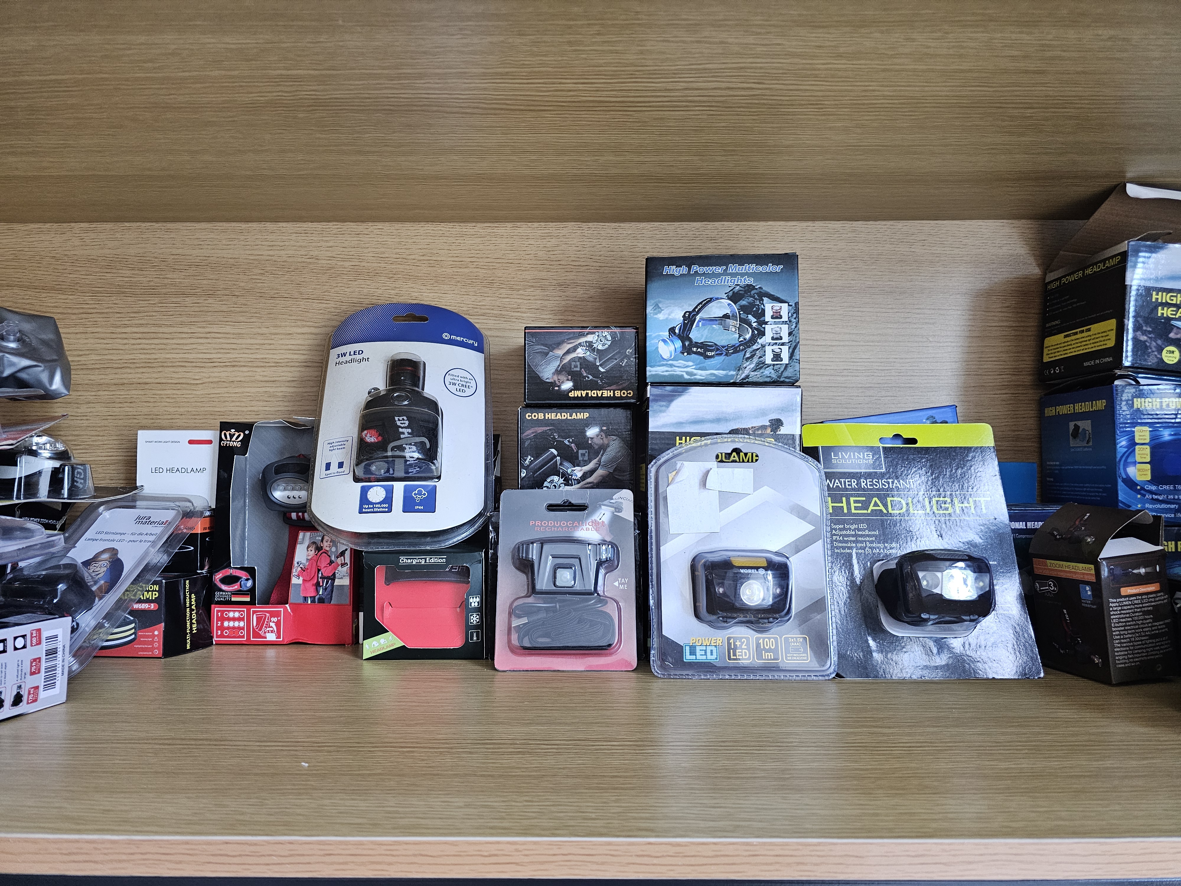 Various packaged LED headlamps, COB headlights, and retail blister boxes neatly displayed on a wooden shelf.