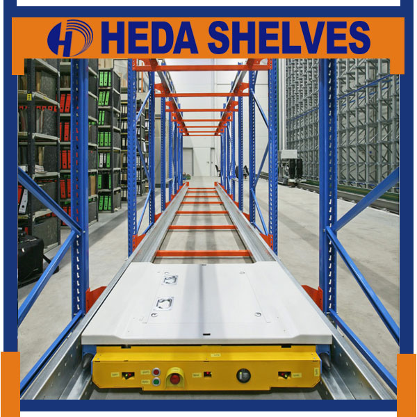 Original HEDA warehouse shuttle rack showing the yellow-front motorized pallet shuttle with a silver top platform, control buttons, twin steel rails, blue braced upright frames and orange cross members