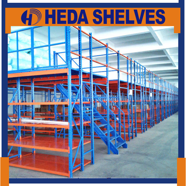 Original HEDA No.00293 long multi-level warehouse shelving system with blue steel braced frames, solid orange steel storage shelf levels, upper platform supports and an integrated blue stairway
