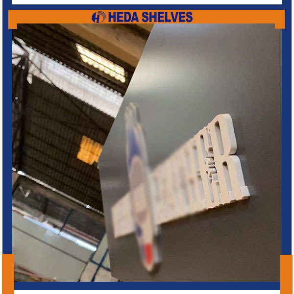 Real close-up of raised light-colored three-dimensional logo lettering mounted on the dark angled header of the HEDA PDS02 pegboard display stand