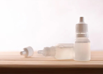 Two plastic eye drop bottles containing eye drops.