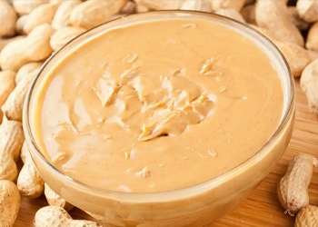 Smooth peanut butter in a glass bowl with whole peanuts, ready-to-use nut spread