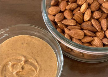 Homemade almond butter next to a bowl of raw almonds, rich natural spread