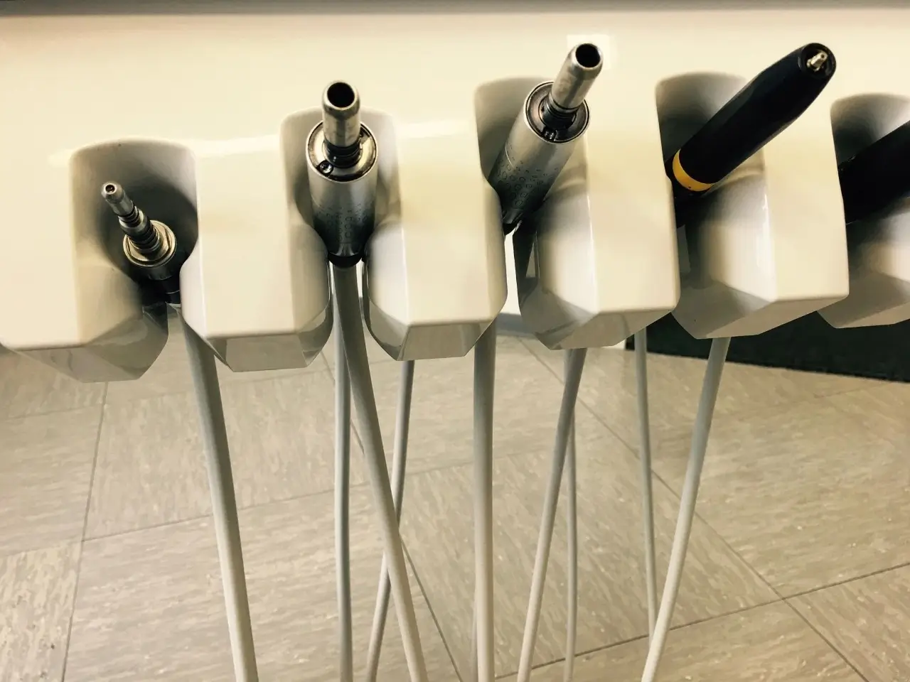 Close-up of dental handpieces and hoses in a dentist's chair unit.