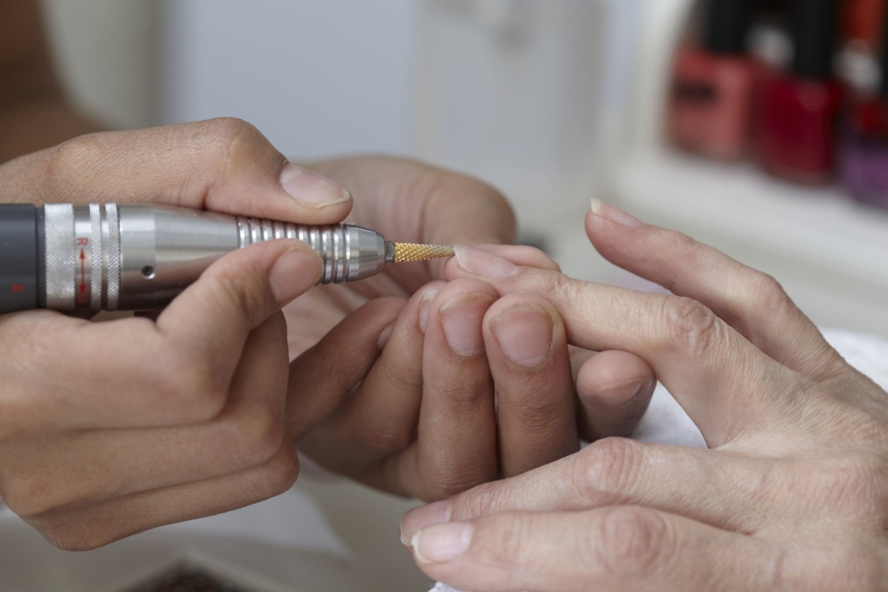 Close up of a manicurist using an electric nail drill to file the cuticle and shape the fingernails of a client.