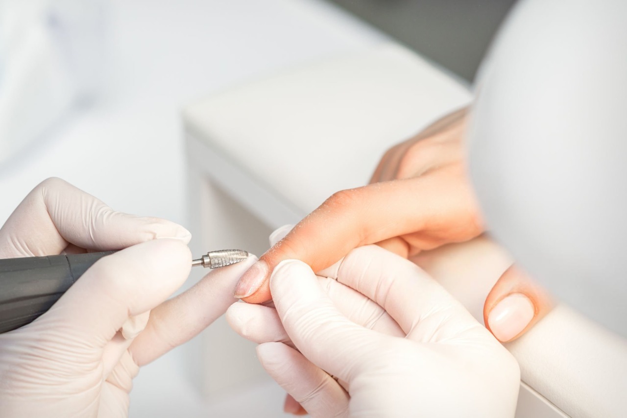 Close up of a manicurist in white gloves using an electric nail drill to groom a client's cuticle and shape the fingernail.
