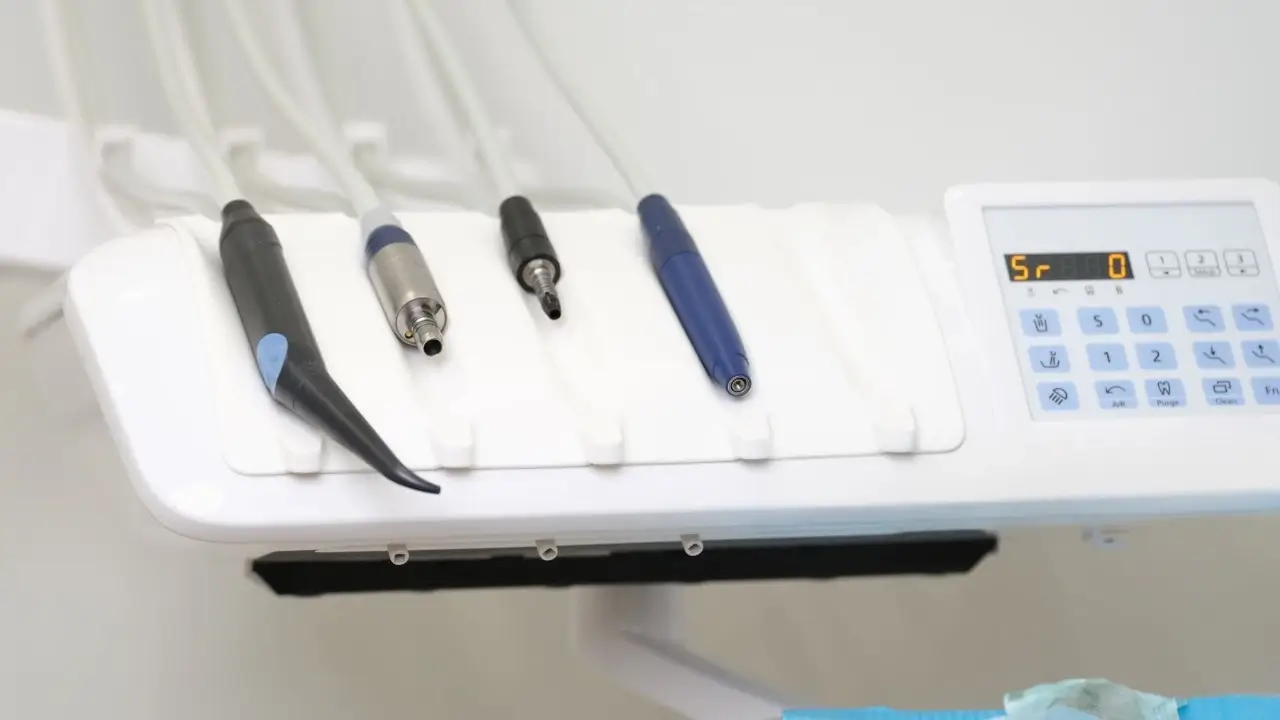 Modern dental unit tray with various handpieces and digital control panel in a white clinic setting.