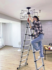a girl is standing on a aluminium telescopic ladder and fixing the light bulbs