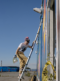 une fille grimpe sur une échelle télescopique pour peindre le mur