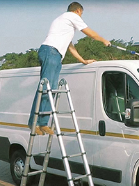 a man standing on a double telescopic ladder is cleaning his vehicle