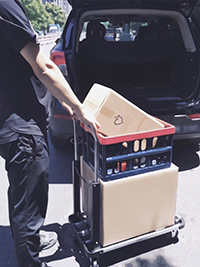 A man is pushing a foldable push cart with many things taking from the trunk of his car