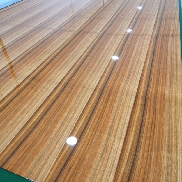 Smooth high-gloss UV-cured wood finish panel, showing reflective surface texture