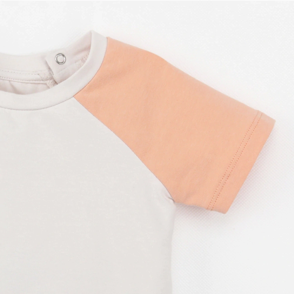 Neck and shoulder close-up of Raglan organic-cotton baby tee with plant-dyed natural powder puff and coral colour (botanical dye)