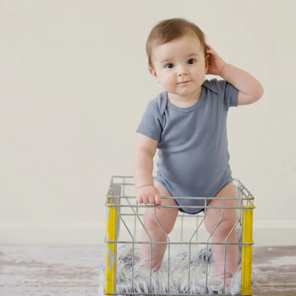Overhead shot of a infant stand in a basket wearing thenatural blue blizzard plant-dyed organic bodysuit