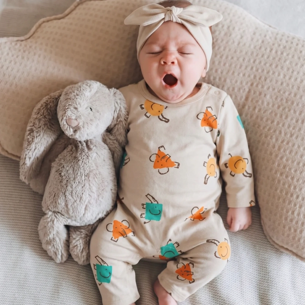 A sleeping infant wearing the natural beige elephant print organic cotton full-body romper, highlighting the comfortable shoulder-snap fit.