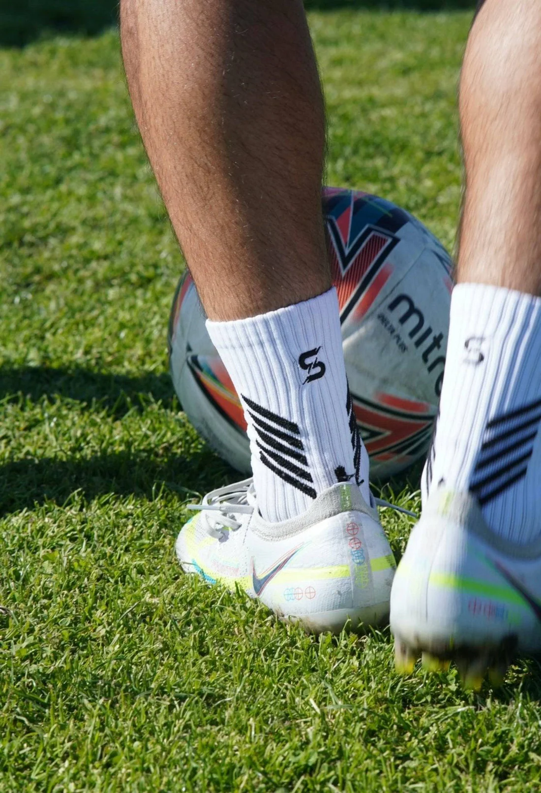 Athlete wearing white crew socks and soccer cleats controlling a football on grass field