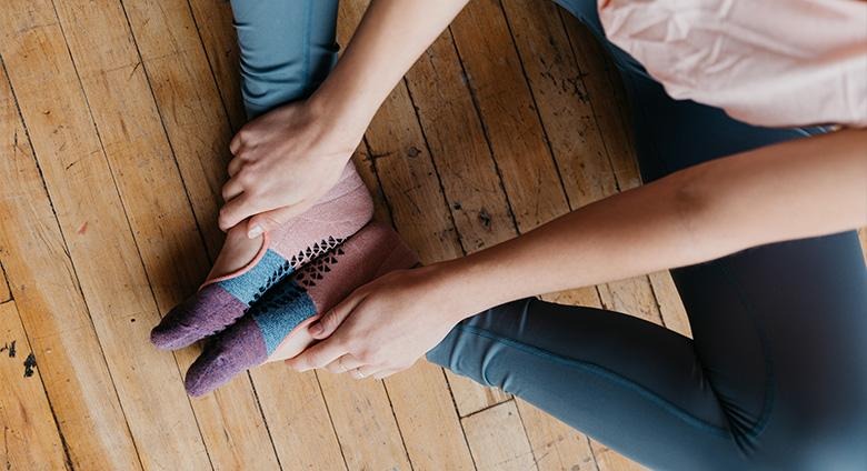Feet wearing grip socks contacting wooden floor during seated stretch position