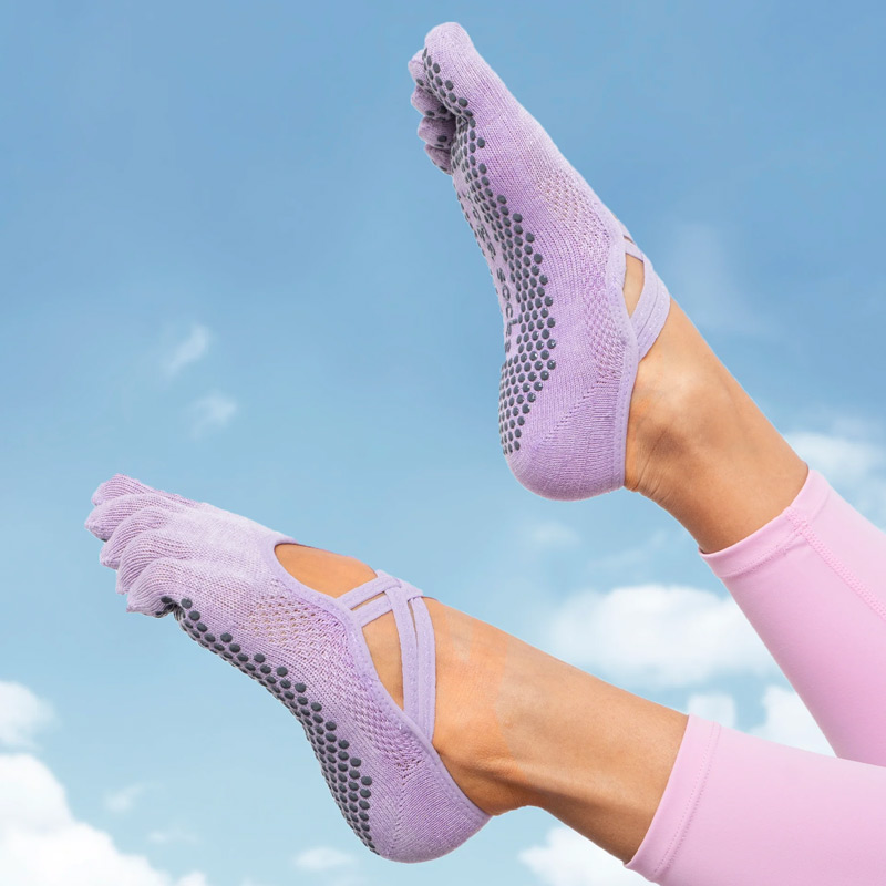 Feet wearing light purple grip socks with dotted traction on the sole, lifted against a blue sky background