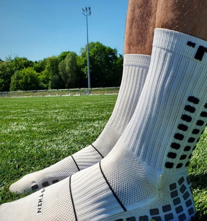 Close-up of white grip socks with silicone traction dots worn on artificial turf, showing ankle and sole grip pattern for stability during sports activity