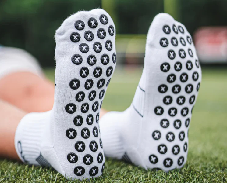 White athletic grip socks with black silicone traction dots on sole, designed for indoor sports and balance training