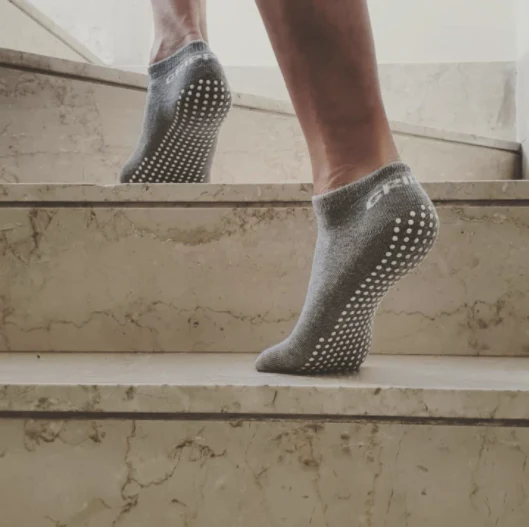 Gray grip socks with silicone anti-slip dots worn while walking up indoor stairs