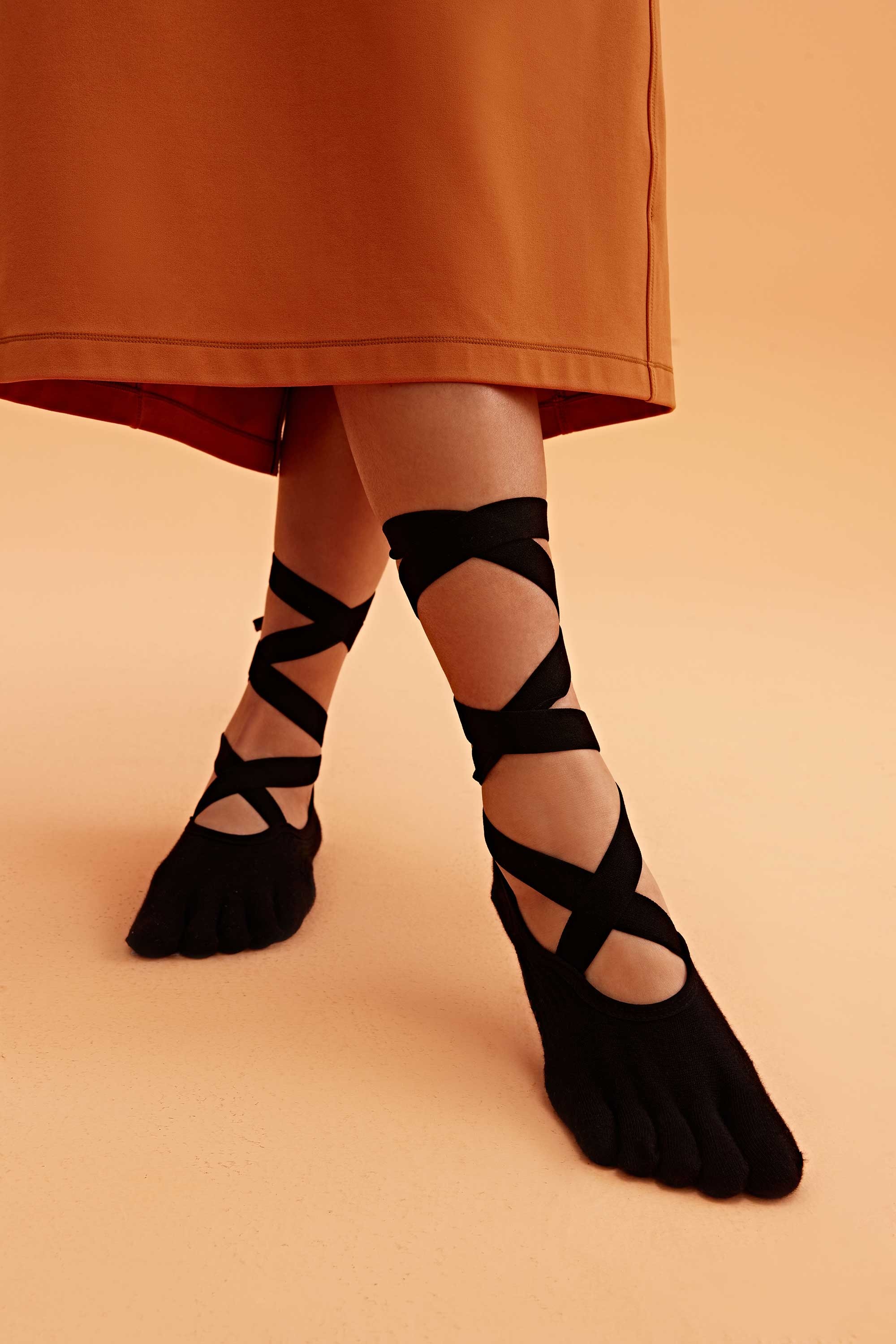 Black five toe grip socks with wrap straps worn for balance and controlled movement on smooth indoor floors