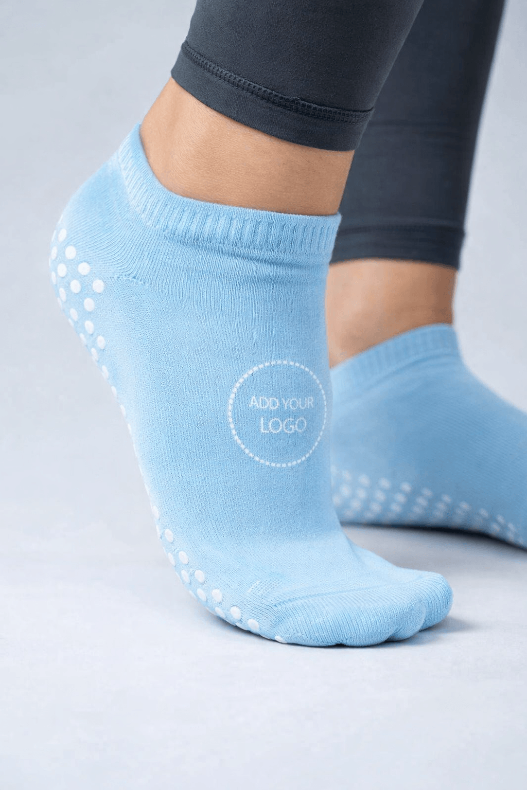 Light blue custom grip socks with non-slip dot pattern and logo placement area, ankle-length design for studio workouts