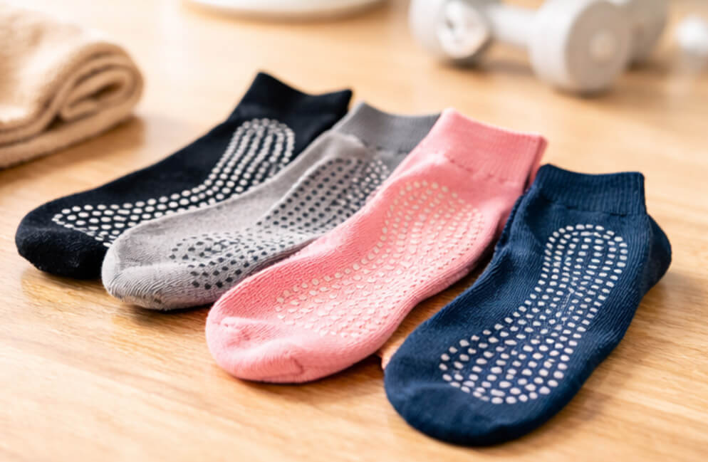 Four colorful non-slip grip socks in black, gray, pink, and navy blue arranged on a wooden floor with silicone grip patterns visible on the soles