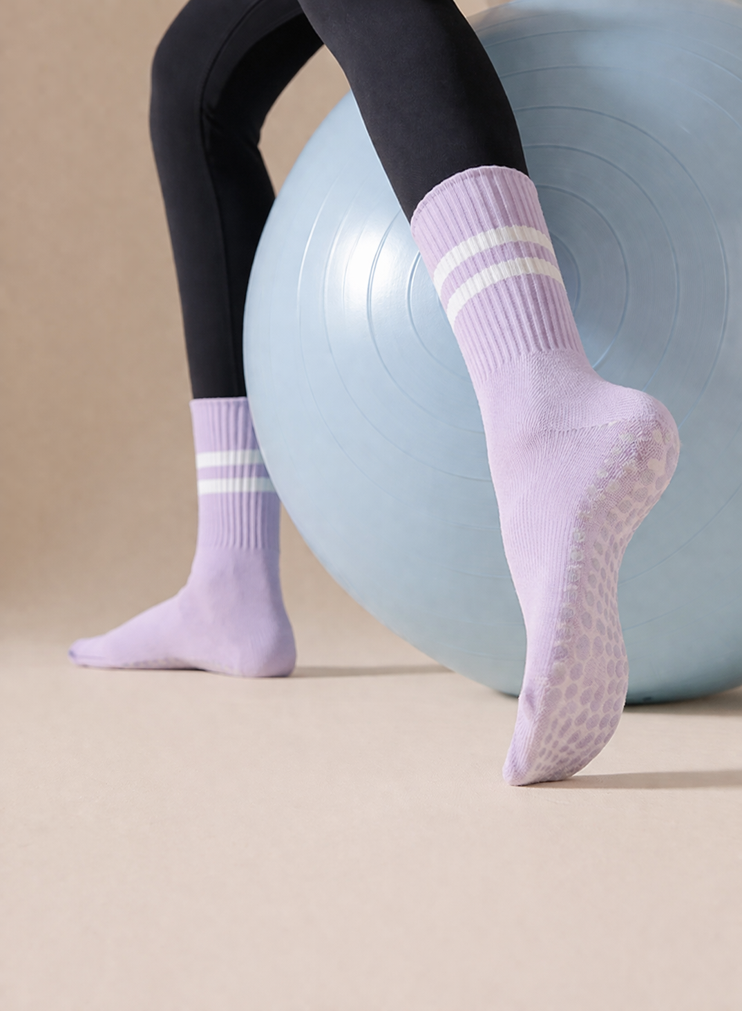 pastel purple wholesale pilates grip socks on feet pressing against exercise ball surface, pilates studio socks supplier scenario