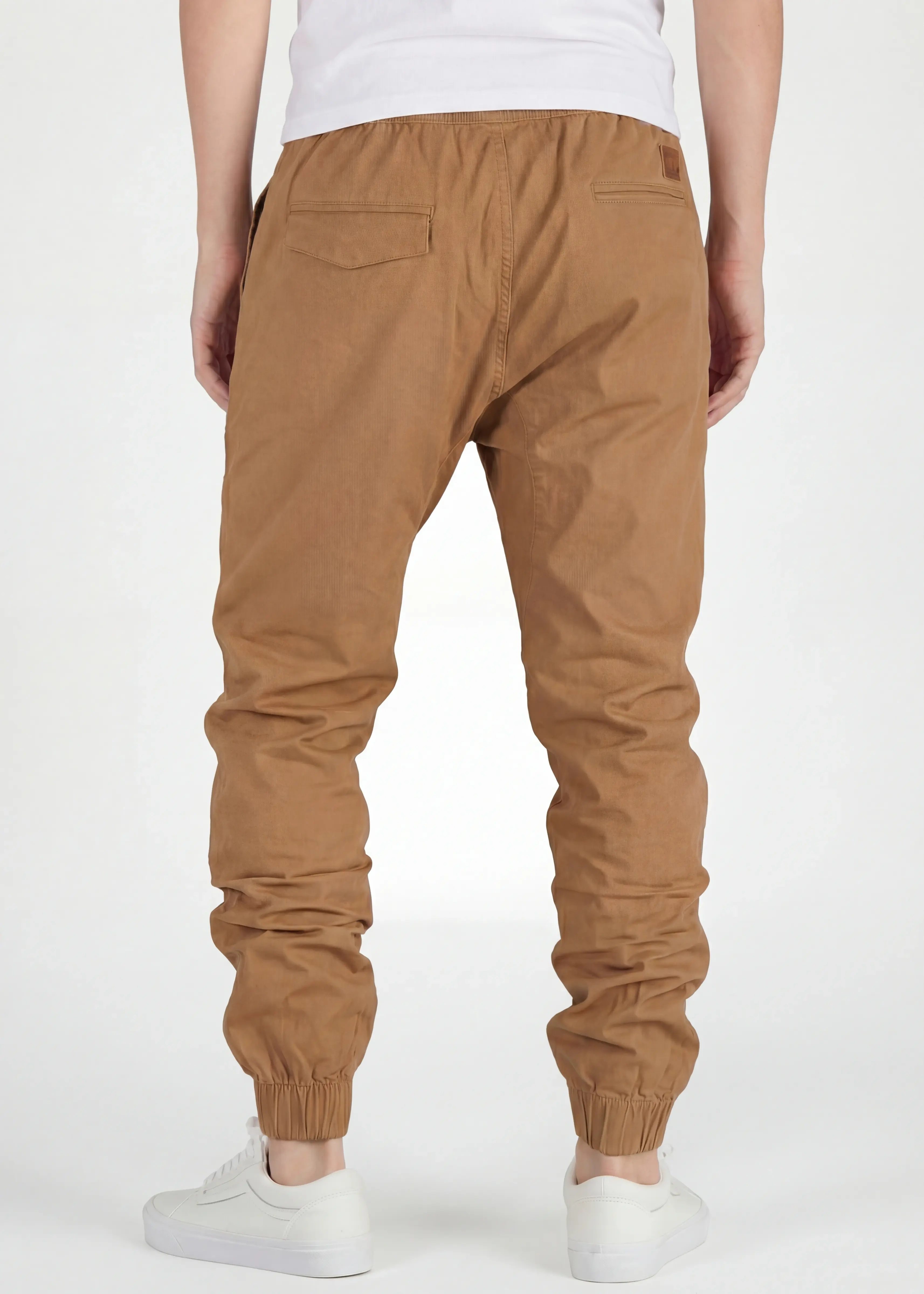 Rear close-up view of ItalyMorn men's tan brown jogger pants, showcasing the clean tailored seat, functional back pockets with flap detail, and secure ribbed ankle cuffs. Paired with white sneakers
