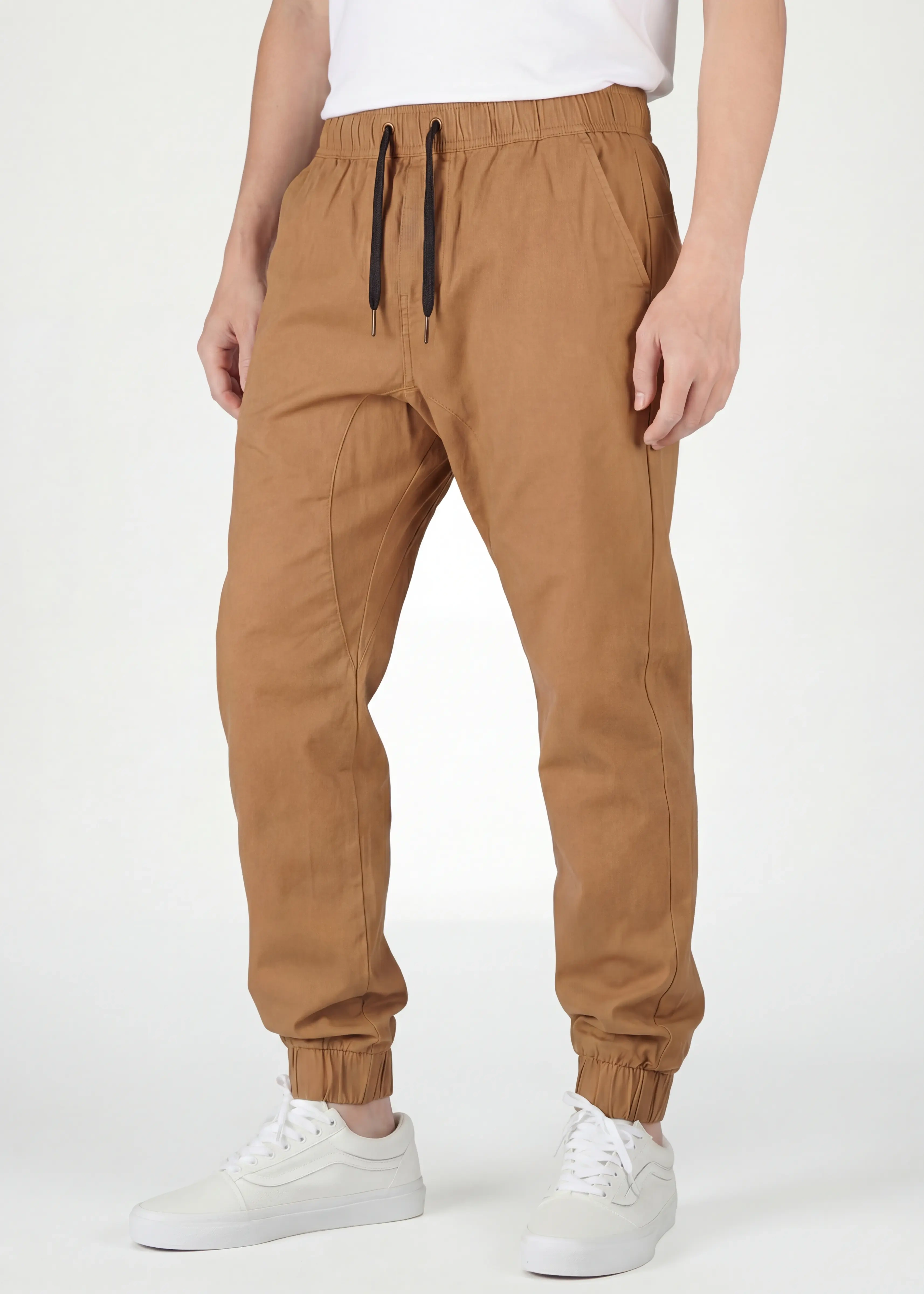 Close-up front view of ItalyMorn men's light brown jogger pants on a model, highlighting the comfortable elastic waistband with black drawstrings, deep side pockets, and modern slim-tapered fit. Paired with white sneakers