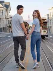 A young couple holding hands and looking back while standing on cable car tracks in San Francisco, with the man wearing a casual grey t-shirt and ItalyMorn men's dark grey jogger pants, illustrating a stylish look for city travel