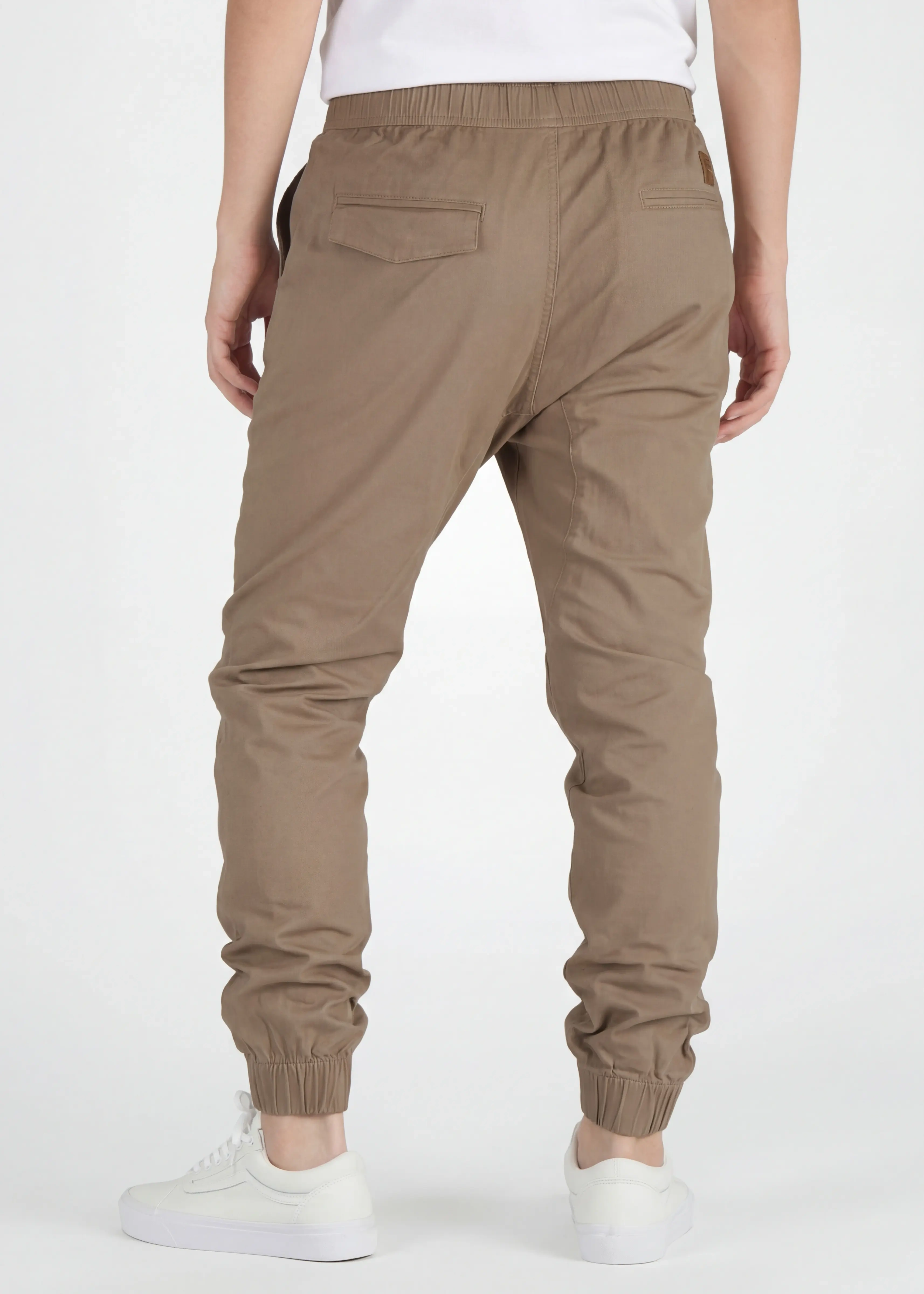 A rear view close-up of ItalyMorn men's dark khaki jogger pants on a model, highlighting the functional back pockets, clean fit, and durable fabric texture. Paired with white sneakers