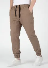 A detailed three-quarter front view of ItalyMorn men's dark khaki jogger pants, emphasizing the relaxed yet tailored fit and the smooth drape of the fabric. A model with hands in pockets against a plain background, wearing white sneakers.